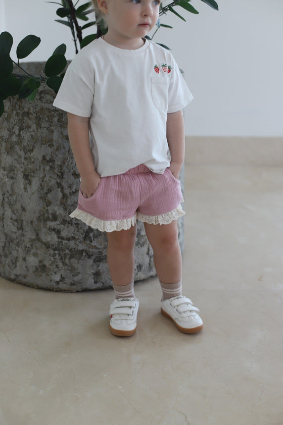 GINGI Girl Short Dust Pink Gabriella - Baby Girl Wearing Pink Muslin Cotton Shorts with Lace Ruffle Standing Front View